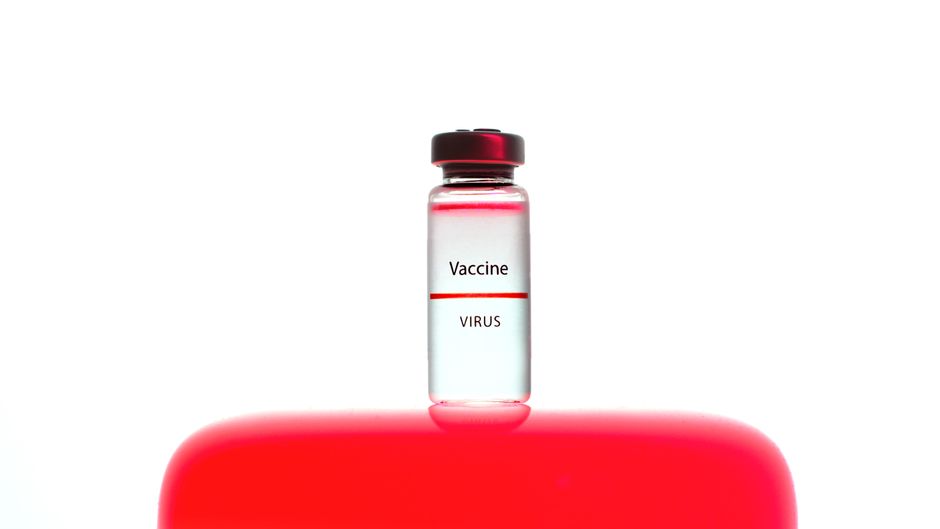 Acercamiento de un vial de vacuna etiquetado sobre un fondo rojo vibrante.