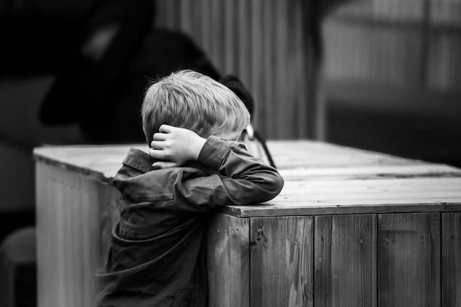 Imagen en blanco y negro de un niño apoyado pensativo en una superficie de madera, que evoca la soledad urbana.