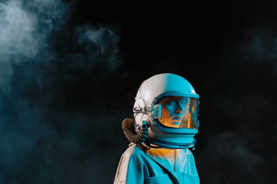 Un retrato dramático de una mujer vestida con un traje espacial y casco en un entorno oscuro y lleno de humo.