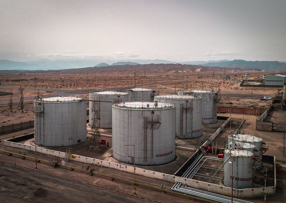 Vista aérea de grandes tanques de petróleo industriales en un entorno desértico con montañas en la distancia.