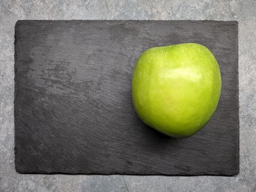 Una manzana Granny Smith fresca colocada sobre una tabla de pizarra oscura, mostrando simplicidad y frescura.