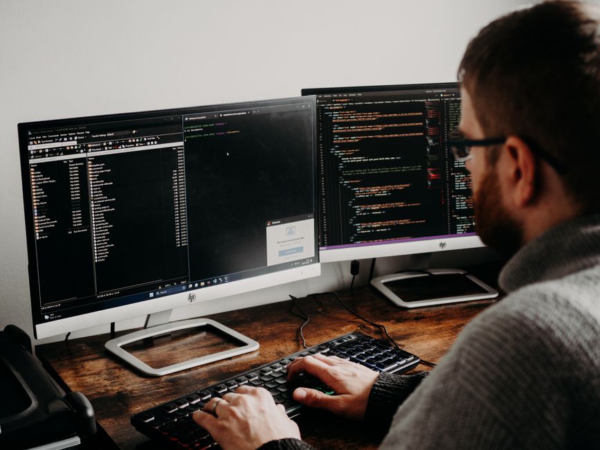 Desarrollador de software escribiendo código en monitores duales en un escritorio de madera.