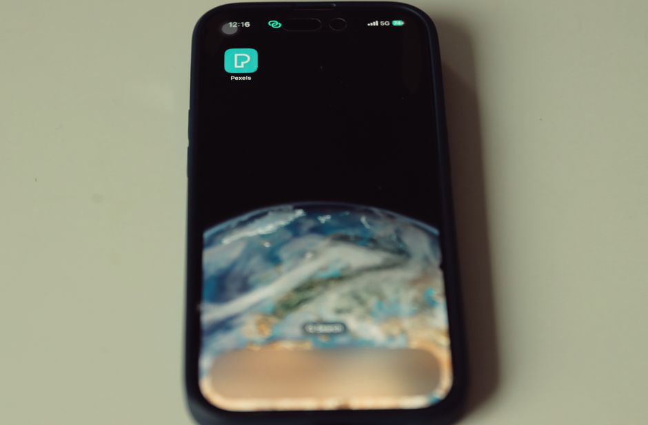 Primer plano de smartphone mostrando fondo de pantalla de la Tierra e ícono de la aplicación Pexels en la pantalla.