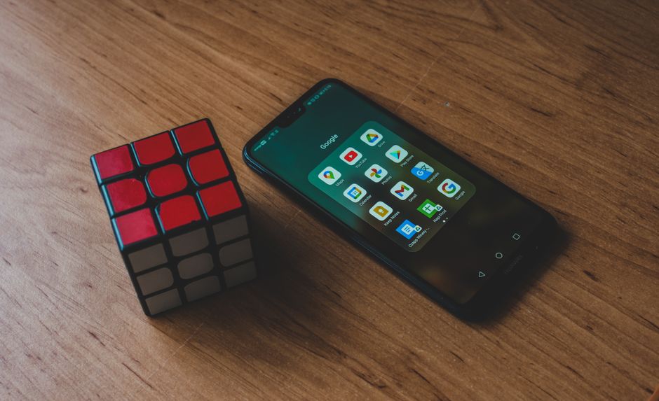 Primer plano de un smartphone con aplicaciones y un Cubo Rubik sobre una mesa de madera. Ideal para temas de tecnología y ocio.