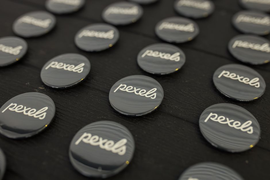 Una vista de cerca de varios botones del logotipo de Pexels dispuestos cuidadosamente sobre una superficie oscura.