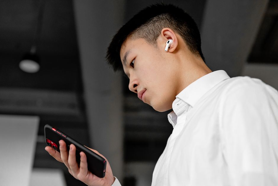 Vista lateral de un joven con auriculares inalámbricos utilizando un smartphone en interiores.