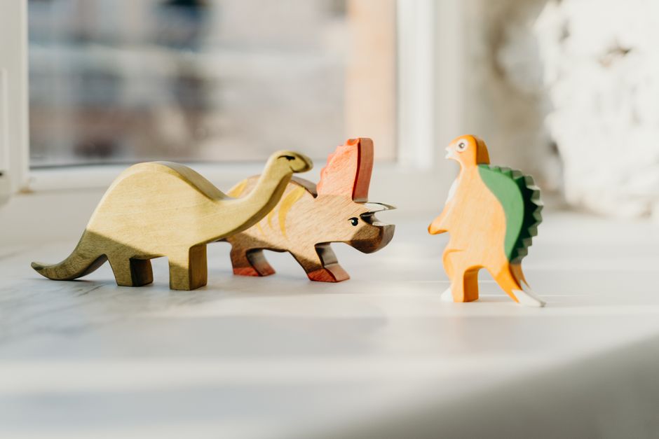 Tres juguetes de dinosaurios de madera en un alféizar de ventana iluminado por el sol, mostrando una escena juguetona.