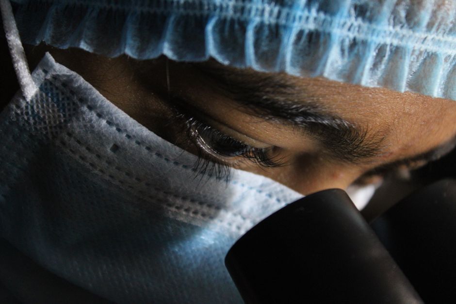 Un científico con equipo de protección observa atentamente a través de un microscopio.