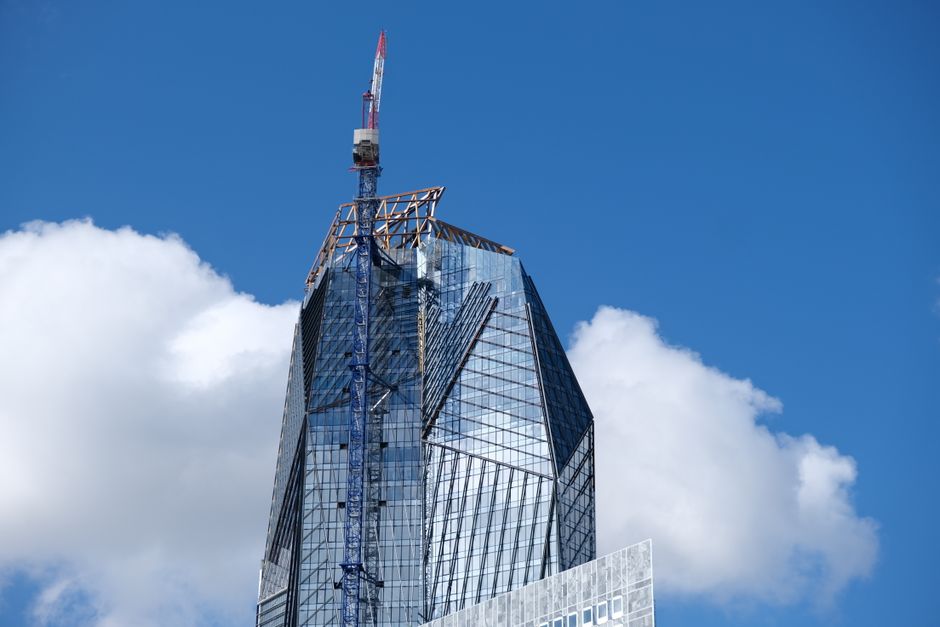 Un rascacielos moderno en un entorno urbano, con arquitectura de vidrio y una grúa de construcción bajo un cielo azul claro.