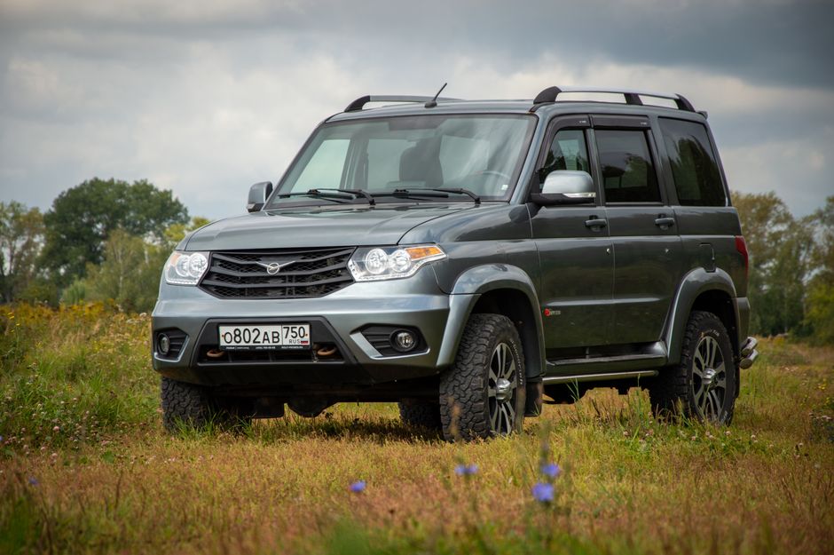 SUV UAZ plateado aparcado en un pintoresco prado rural, mostrando su diseño robusto.