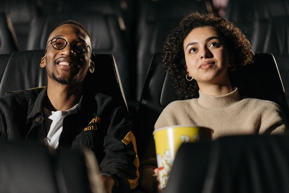 Pareja joven sonriente viendo una película en el cine, compartiendo palomitas.