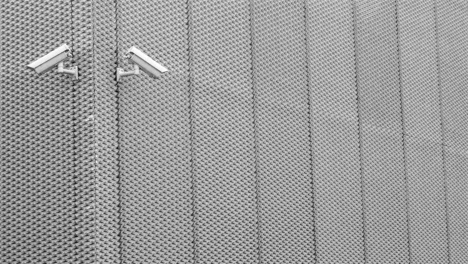 Dos cámaras de vigilancia montadas en una pared de metal texturizada que exhibe arquitectura moderna.