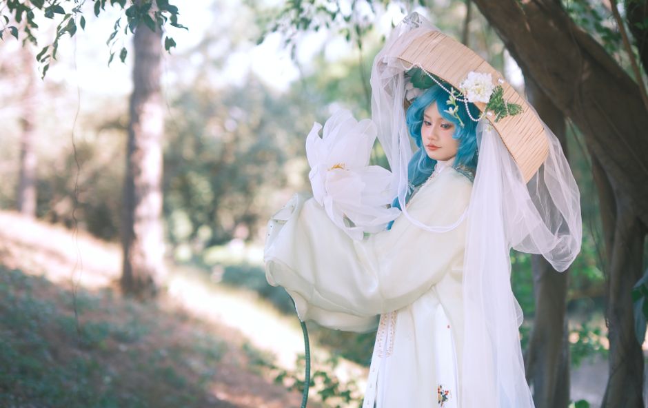 Cosplayer con disfraz elaborado, cabello azul y acentos florales en un entorno natural sereno.