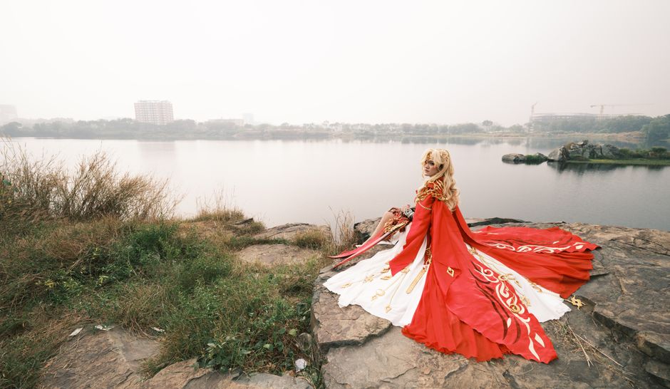 Una mujer con un impresionante vestido de cosplay rojo se sienta junto a un lago tranquilo, exudando elegancia fantástica.