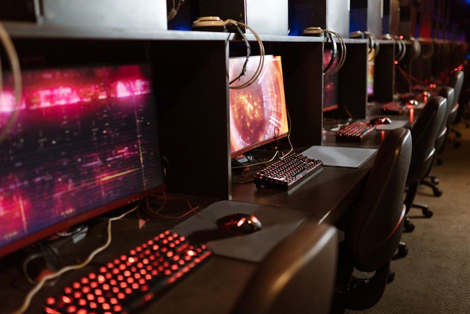 Fila de estaciones de juego con teclados y monitores iluminados en una arena de esports.