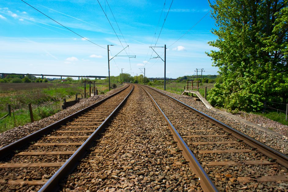 Vista de vías de ferrocarril que se extienden a través del exuberante campo verde del Reino Unido bajo un cielo azul claro.