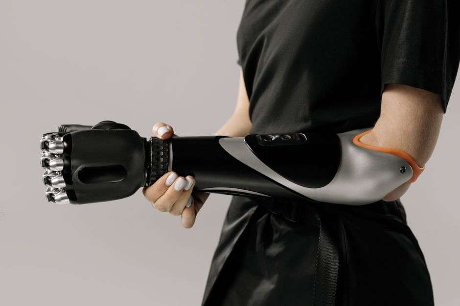 Primer plano de una mujer sosteniendo un elegante brazo protésico negro en un entorno de estudio.
