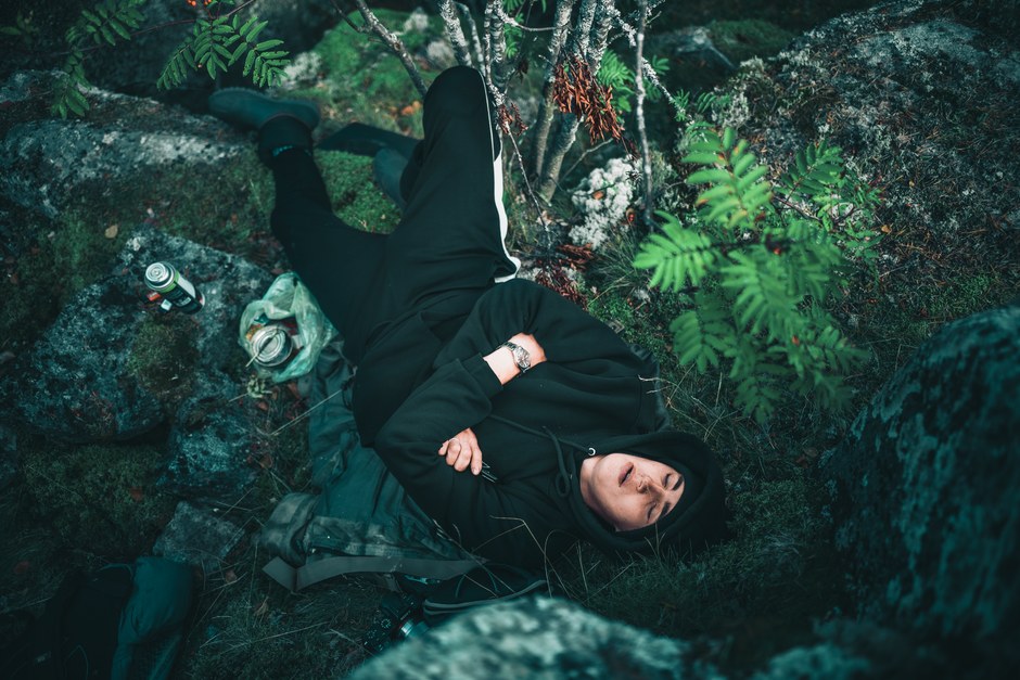 Un hombre con sudadera negra relajándose sobre rocas rodeado de naturaleza en un entorno forestal.