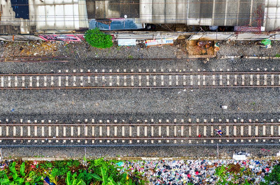 Vista aérea de las vías de tren entre estructuras urbanas y vegetación en Yakarta, Indonesia.