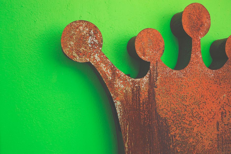 Una corona de hierro oxidado artística contra una pared verde vívida, mostrando textura y contraste.