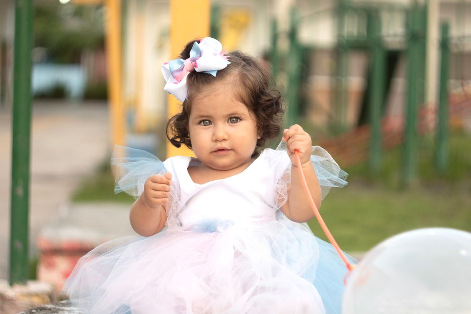 Adorable niña en un vestido blanco y moño, disfrutando del aire libre con un globo.
