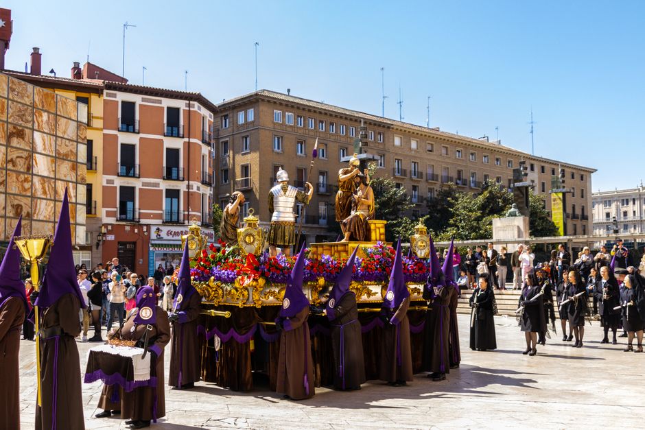 Una vibrante procesión religiosa con trajes y estatuas en Zaragoza, España.