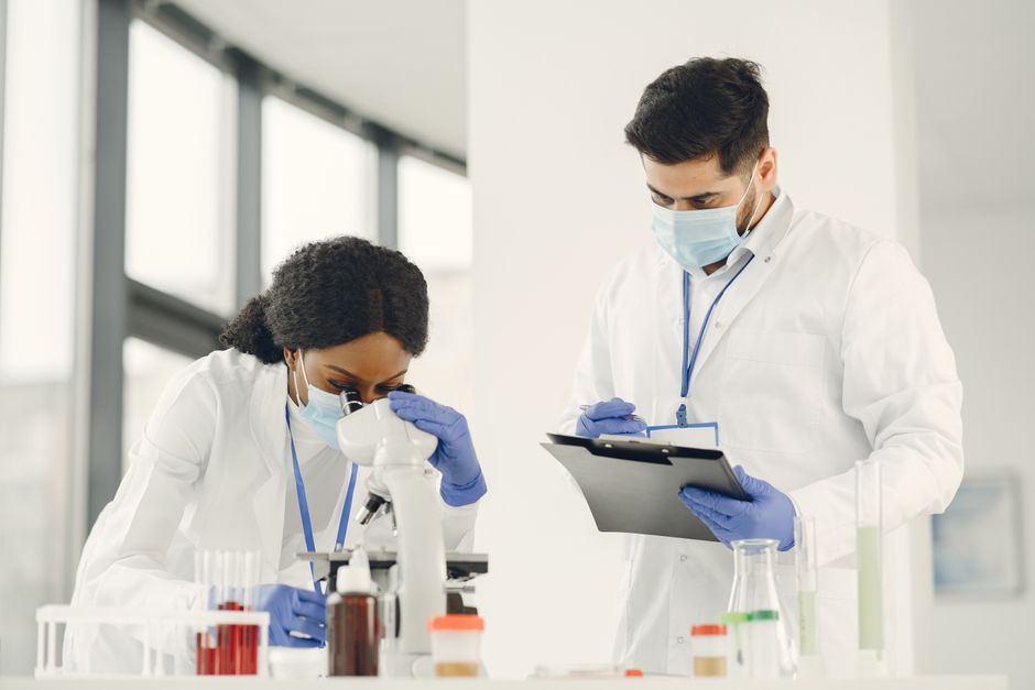 Dos científicos trabajando con un microscopio y una carpeta en un entorno de laboratorio.