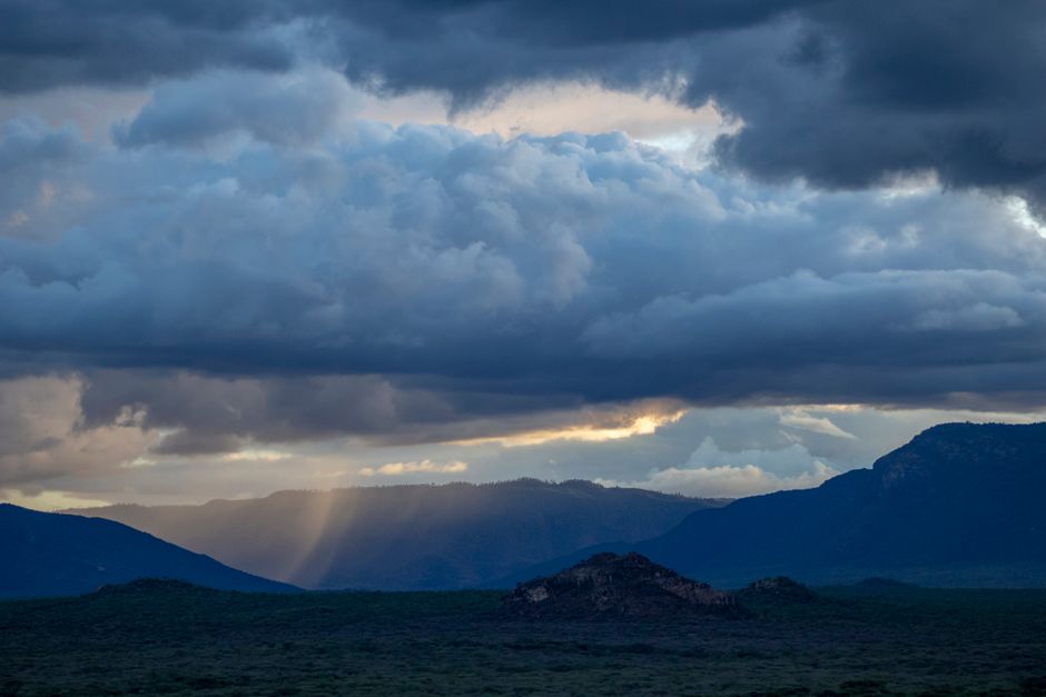 Una vista impresionante de montañas bajo un cielo nublado dramático con la luz del sol filtrándose, mostrando la belleza de la naturaleza.