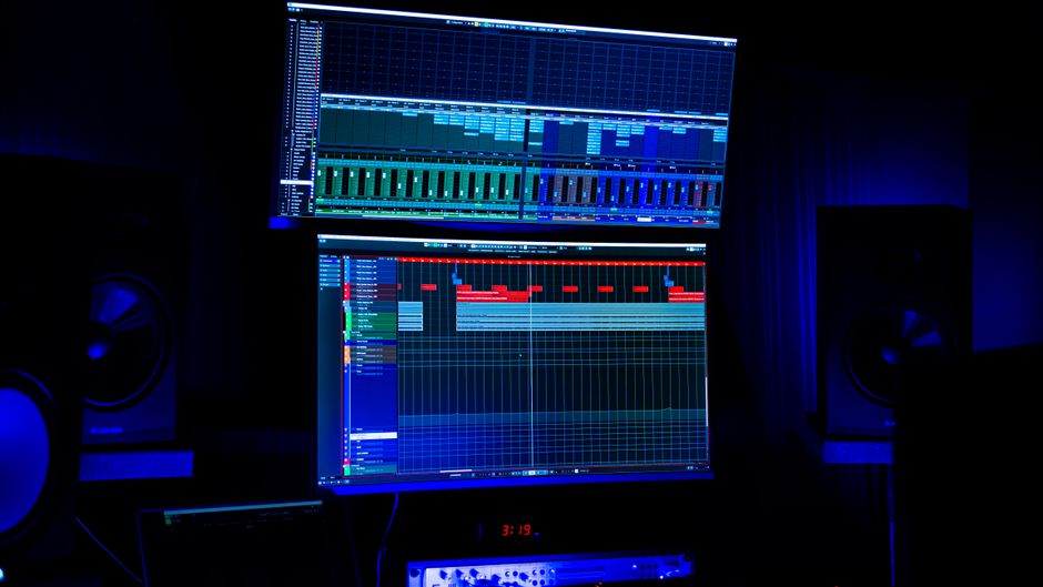 Un estudio de grabación moderno con dos pantallas que muestran software de edición de audio bajo iluminación de neón azul.