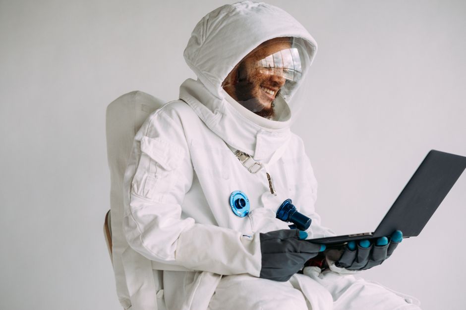 Hombre sonriente en traje de astronauta usando un portátil en el interior. Perfecto para temas de ciencia ficción y tecnología.