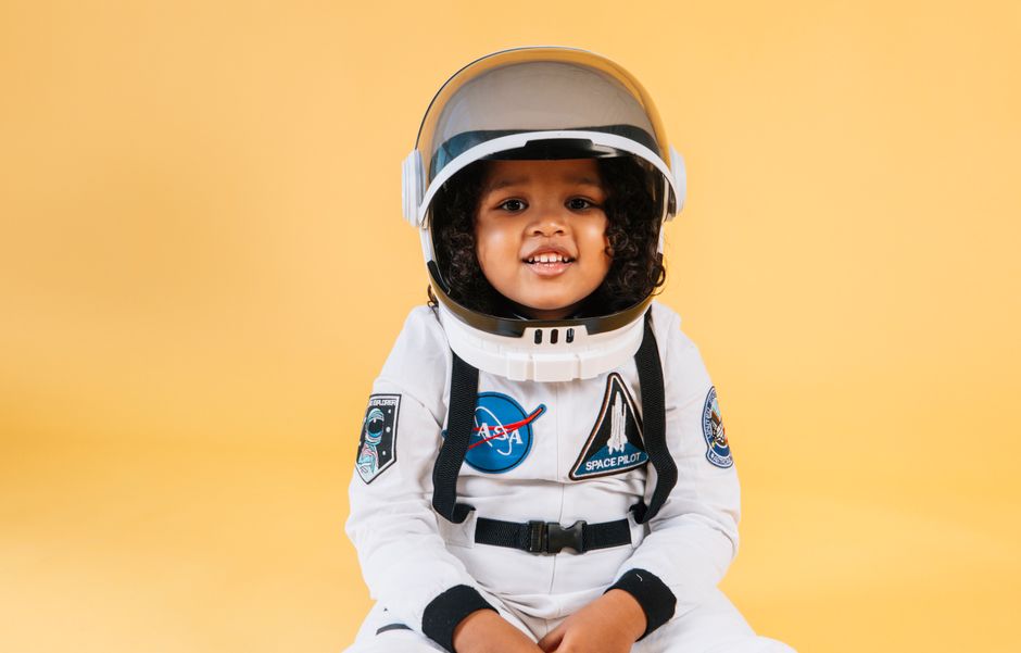 Niño lindo vestido con un traje de astronauta y casco sonriendo contra un fondo amarillo en el estudio.