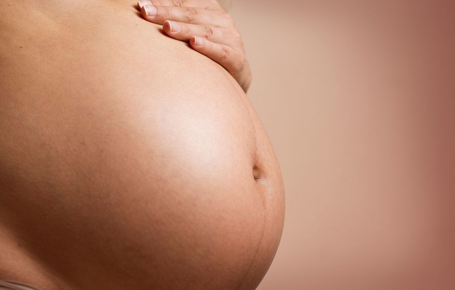 Un primer plano íntimo del abdomen de una mujer embarazada, destacando la maternidad y la paternidad.