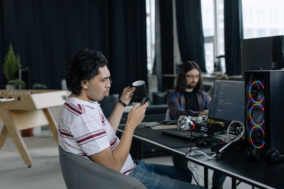 Dos programadores trabajando en una oficina moderna, concentrados en codificar y disfrutando de un descanso para tomar café.