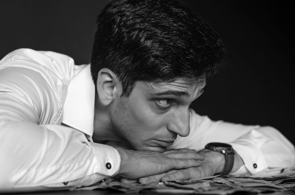 Retrato en blanco y negro de un hombre pensativo descansando en una mesa, vestido con una camisa blanca.