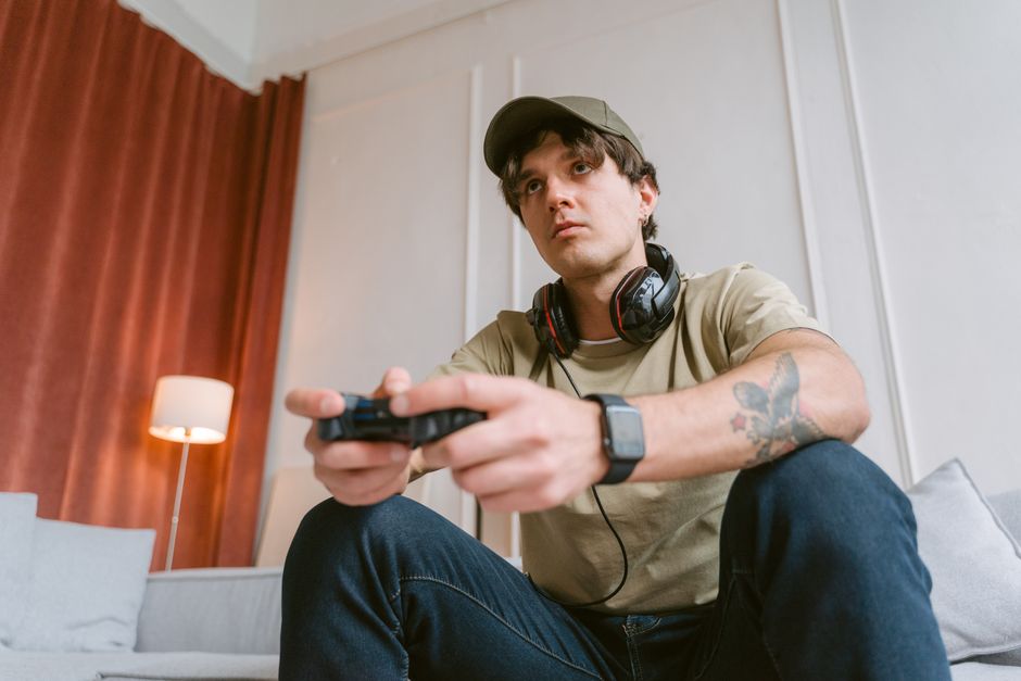 Joven casual con un control de juego y auriculares, concentrado en jugar un videojuego en interiores.