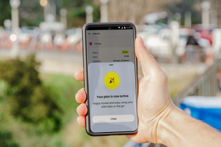 Smartphone mostrando un plan eSIM activo al aire libre, fondo de ciudad desenfocado.