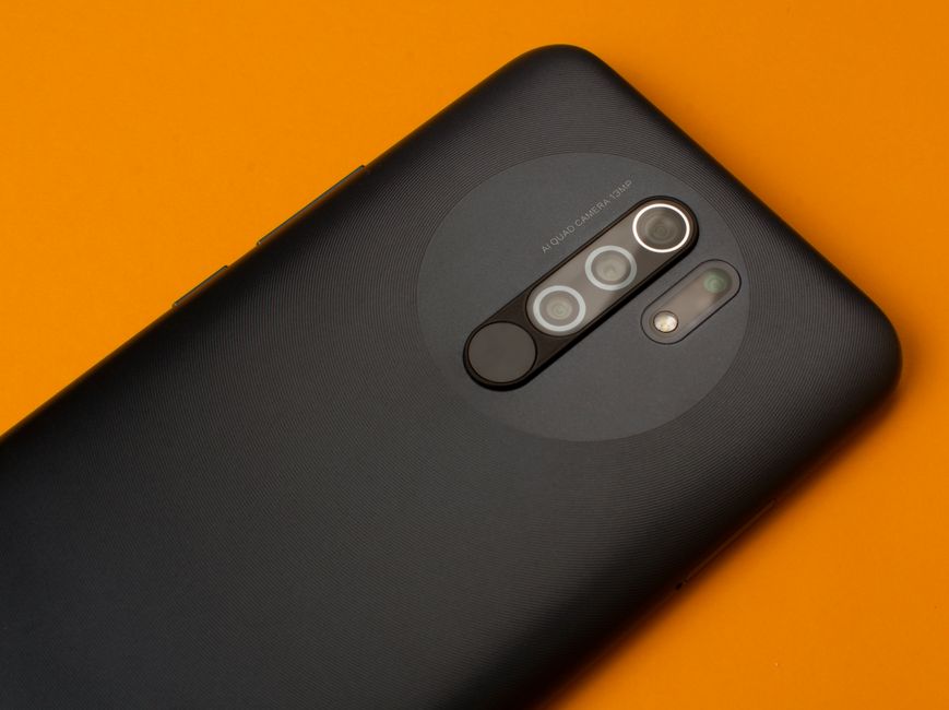 Fotografía en primer plano de la cámara trasera de un smartphone sobre un fondo naranja brillante.