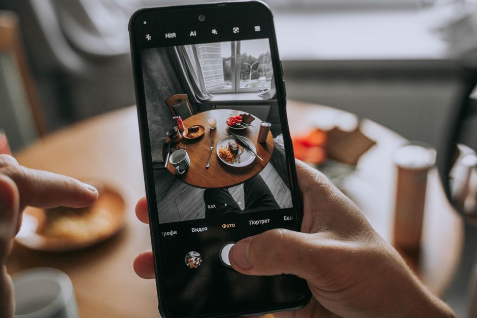 Tomar Una Foto De Una Comida En Una Mesa Con Un Teléfono Inteligente En Un Entorno Acogedor