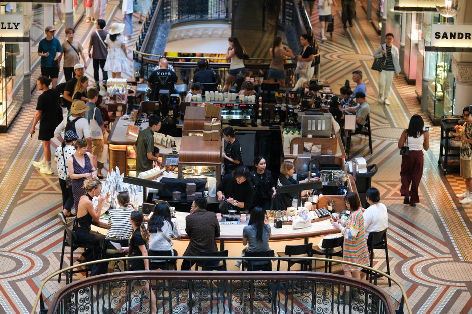 Una cafetería animada dentro de un centro comercial de alto nivel, lleno de visitantes diversos y con una decoración elegante.