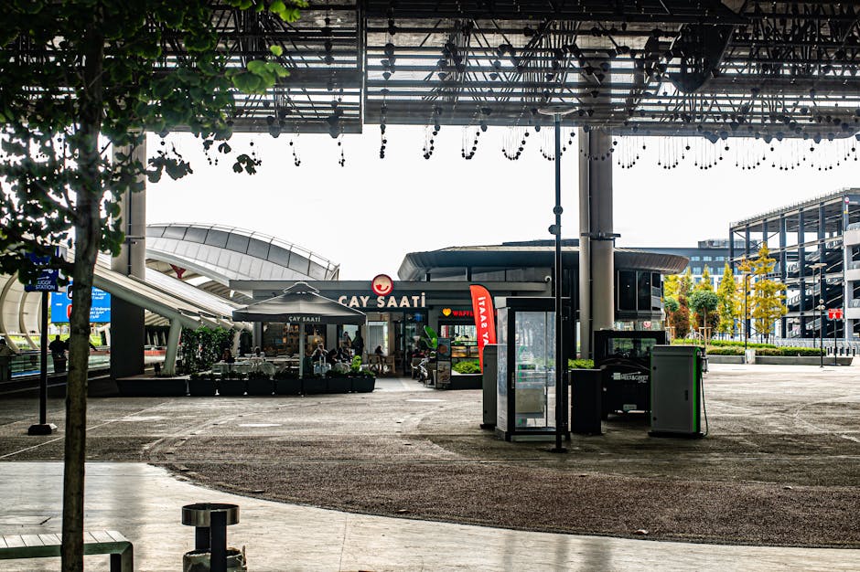 Vista exterior de un café moderno en un entorno urbano animado, con asientos y elementos arquitectónicos únicos.