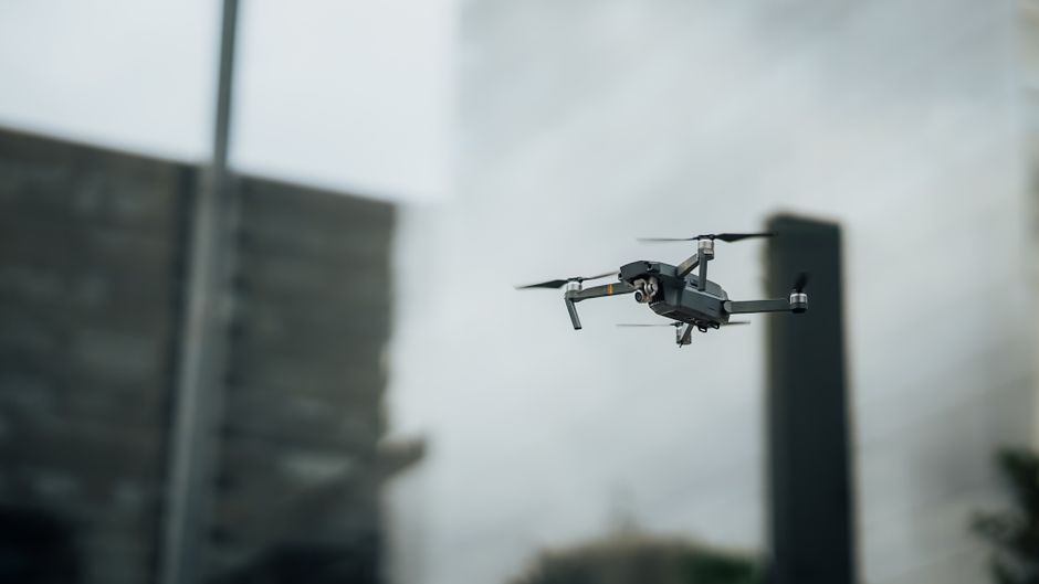 Primer plano de un dron volando entre rascacielos de la ciudad, mostrando tecnología moderna.