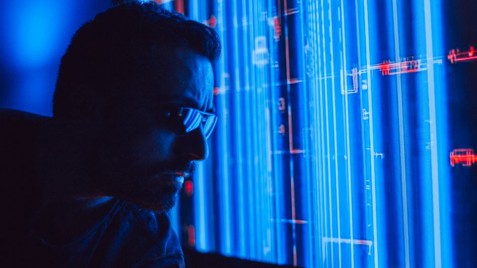 Un hombre con gafas de sol estudia atentamente una pantalla holográfica azul vibrante, simbolizando tecnología digital.