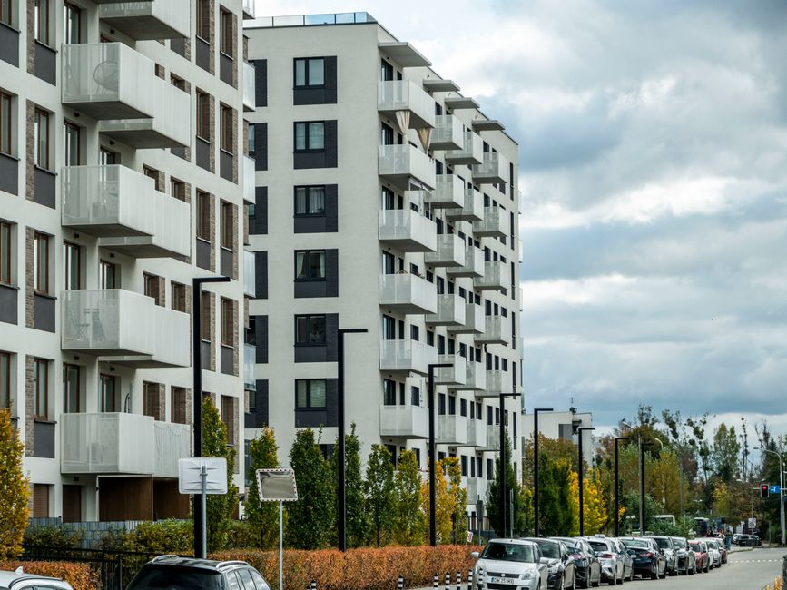 Complejo de apartamentos contemporáneo en una calle de la ciudad con coches estacionados y follaje otoñal.