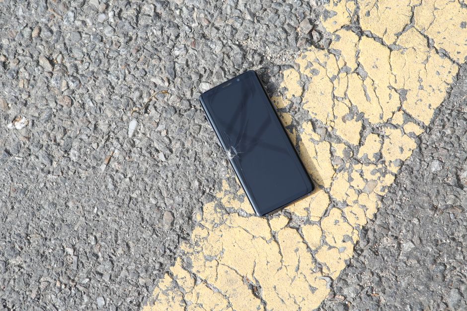 Una vista en primer plano de un smartphone agrietado acostado en una carretera de asfalto iluminada por el sol.