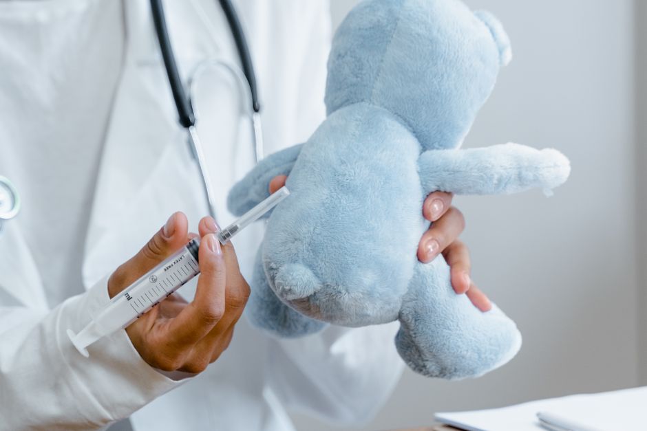 Primer plano de un médico utilizando una jeringa en un juguete de peluche con fines educativos.