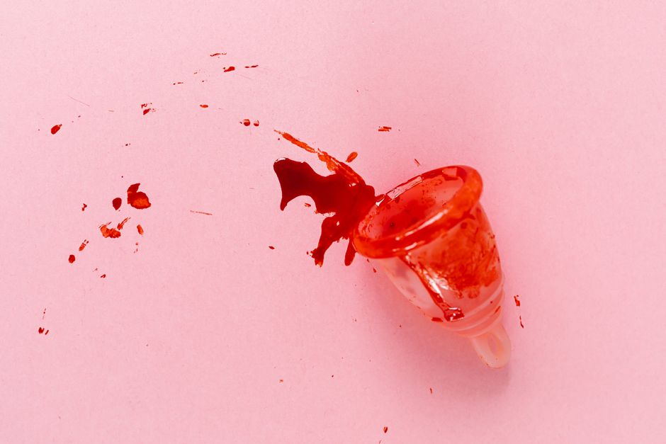 Una copa menstrual con sangre derramada sobre una superficie rosa, simbolizando la menstruación y la salud de las mujeres.