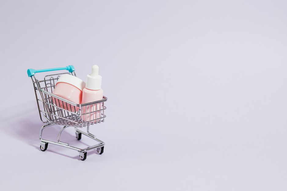Pequeño carrito de compras con productos de cuidado de la piel en rosa sobre un fondo pastel.