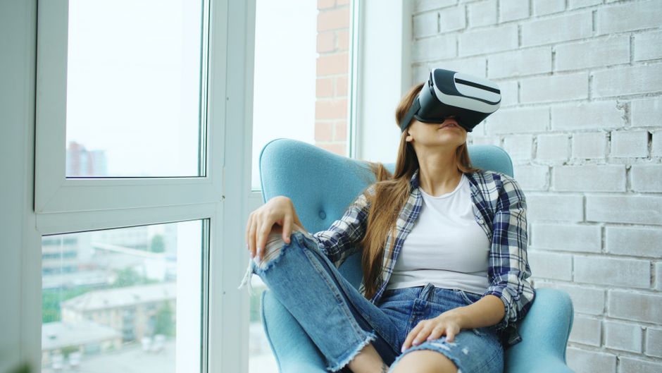 Mujer informal con gafas de realidad virtual sentada en una habitación moderna, con aspecto relajado y absorta en la realidad virtual.