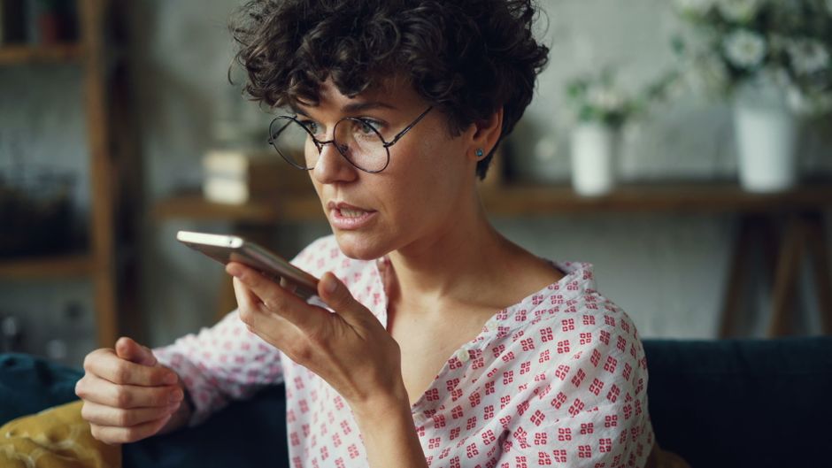 Mujer informal usando comandos de voz en su teléfono inteligente en casa.