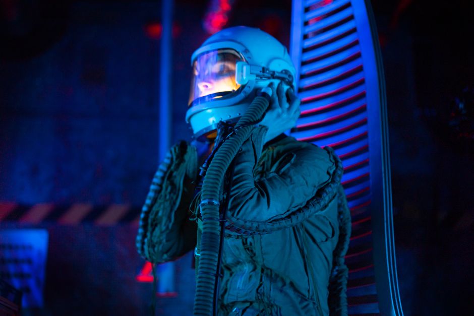 Una persona en un traje espacial explora una nave espacial futurista con iluminación azul, transmitiendo una atmósfera de ciencia ficción.